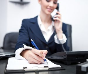 businesswoman using phone, taking notes at office desk