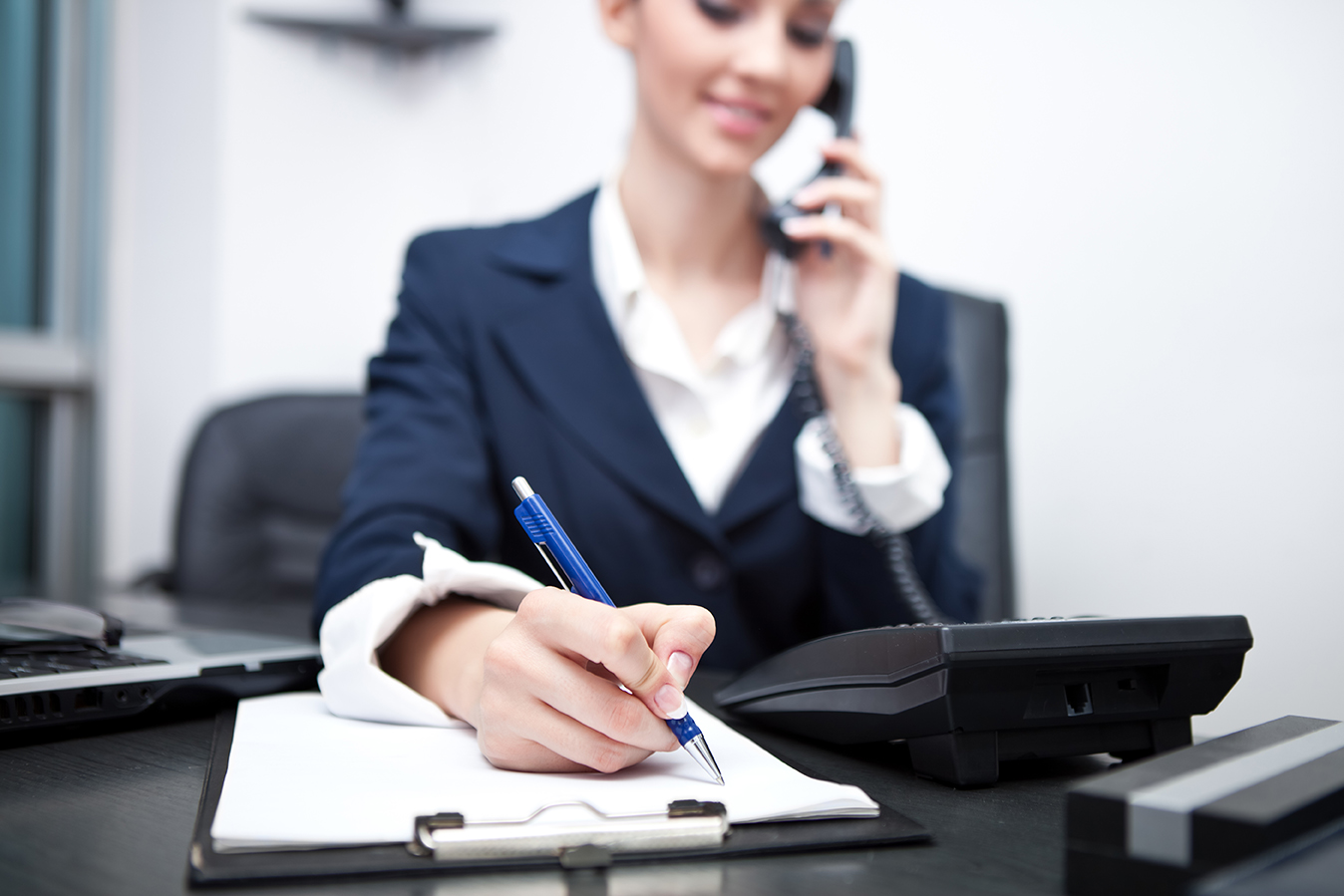 businesswoman using phone, taking notes at office desk